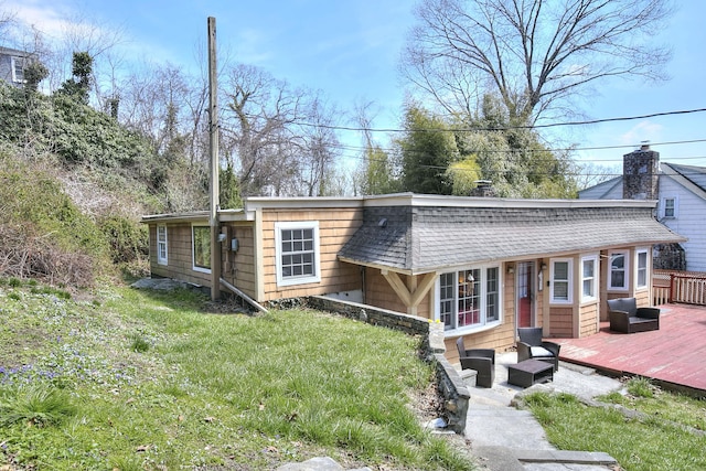 rear view of property featuring a deck, outdoor lounge area, roof with shingles, and a yard
