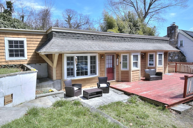 rear view of house with a deck, roof with shingles, and a chimney