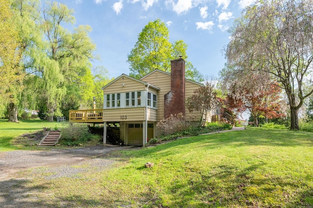 rear view of house featuring dirt driveway, a chimney, a carport, a wooden deck, and a lawn