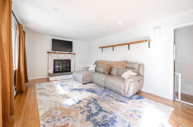 living area with wood finished floors, a brick fireplace, and baseboards
