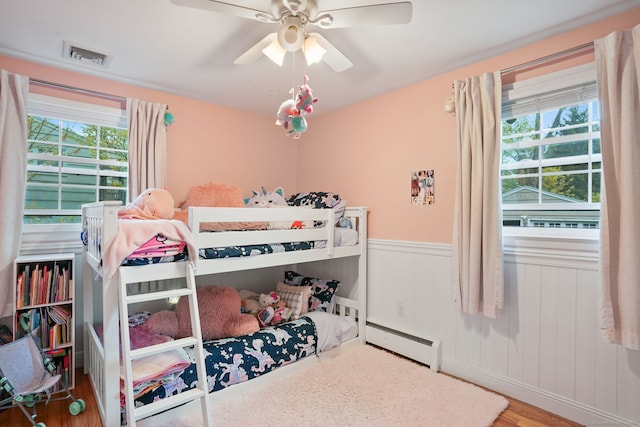 bedroom featuring a baseboard heating unit, a wainscoted wall, visible vents, and multiple windows