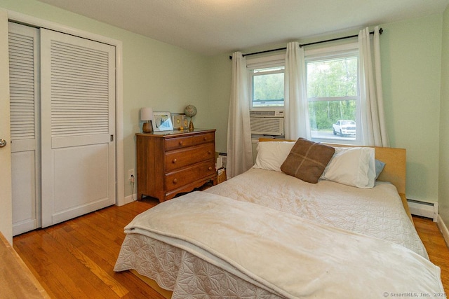bedroom with baseboard heating, wood finished floors, a closet, and cooling unit