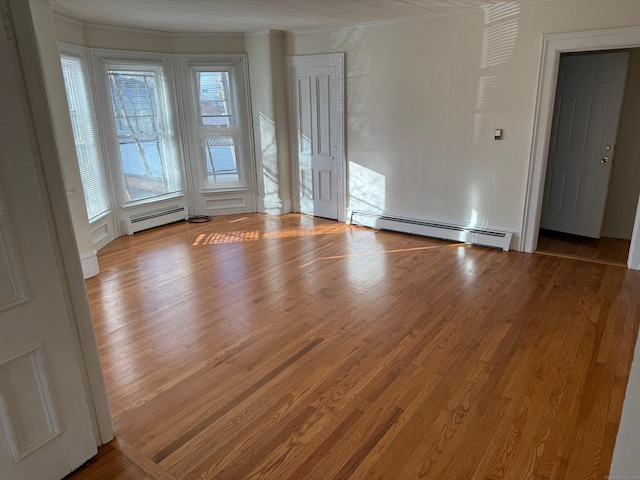 spare room with crown molding, wood finished floors, and baseboard heating