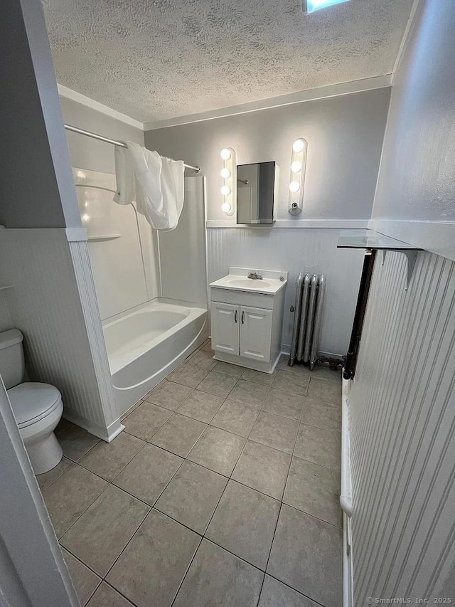full bathroom featuring toilet, radiator heating unit, a textured ceiling, tile patterned flooring, and wainscoting