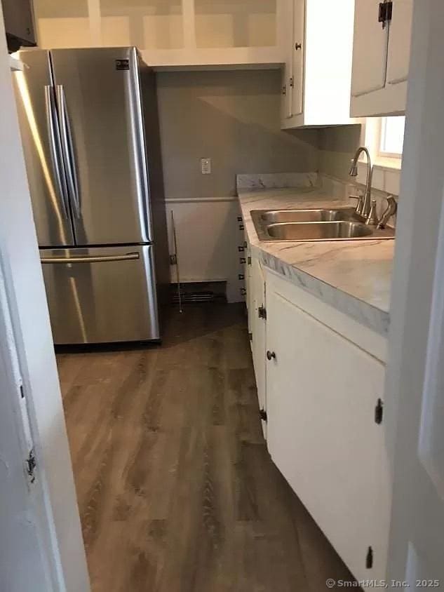 kitchen with a sink, freestanding refrigerator, white cabinetry, and light countertops