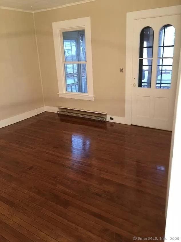 empty room with a baseboard heating unit, dark wood-style flooring, ornamental molding, and baseboards