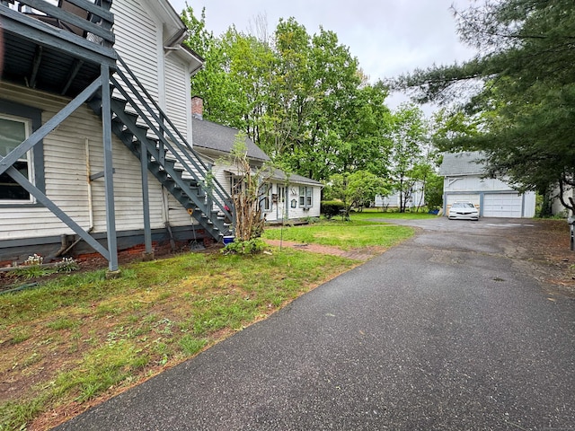 view of property exterior with stairs, a chimney, a lawn, an outbuilding, and a detached garage