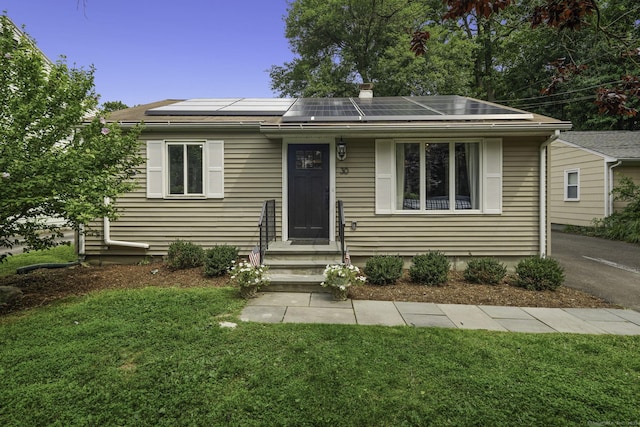 view of front of home with roof mounted solar panels, a front yard, a chimney, and entry steps
