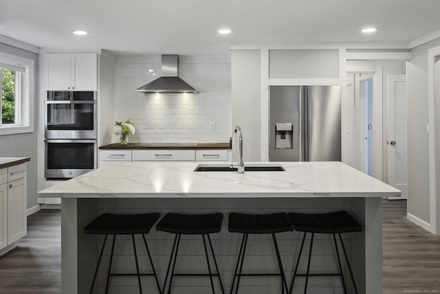 kitchen with appliances with stainless steel finishes, wall chimney range hood, a sink, decorative backsplash, and white cabinetry