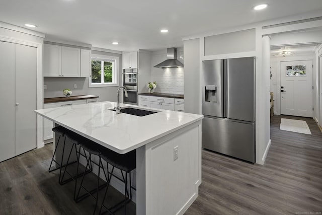 kitchen with appliances with stainless steel finishes, wall chimney range hood, a sink, dark wood-style floors, and decorative backsplash
