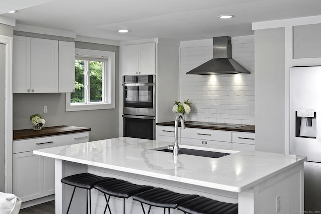 kitchen featuring a sink, wall chimney range hood, tasteful backsplash, recessed lighting, and appliances with stainless steel finishes