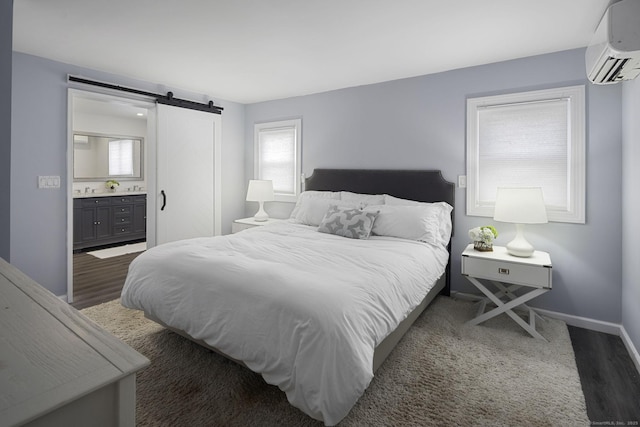 bedroom with a wall mounted air conditioner, a barn door, baseboards, ensuite bathroom, and wood finished floors