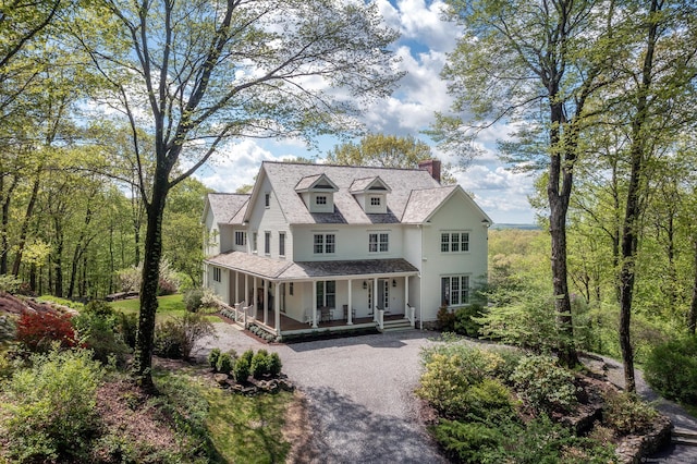 view of front of property with a porch, a chimney, driveway, and a shingled roof