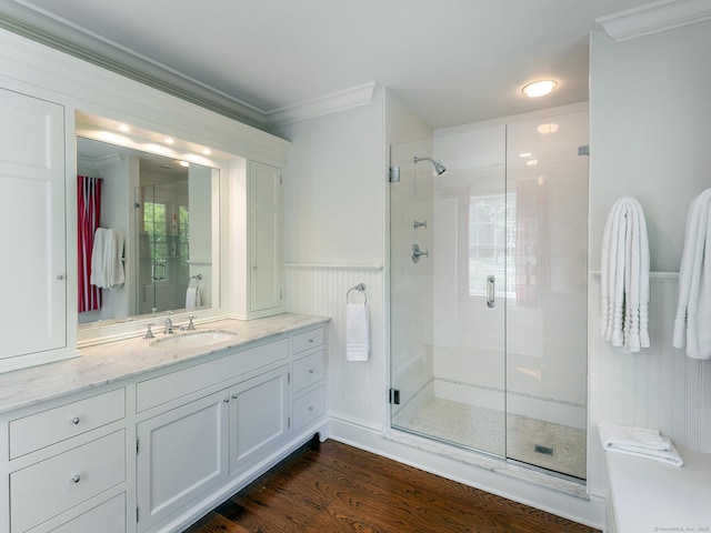 full bath featuring ornamental molding, a shower stall, vanity, wood finished floors, and a wainscoted wall