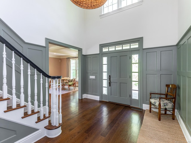 entrance foyer with a decorative wall, stairway, dark wood-style flooring, and a high ceiling