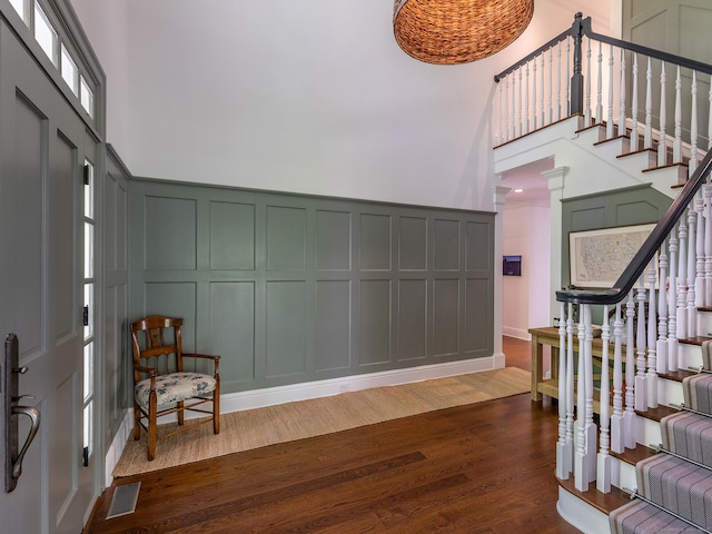 entrance foyer with a decorative wall, a towering ceiling, dark wood-style floors, and stairway