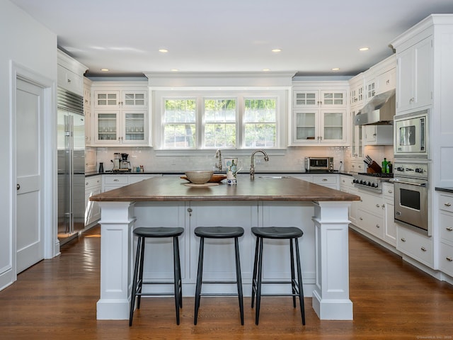 kitchen with built in appliances, dark countertops, an island with sink, a breakfast bar area, and recessed lighting