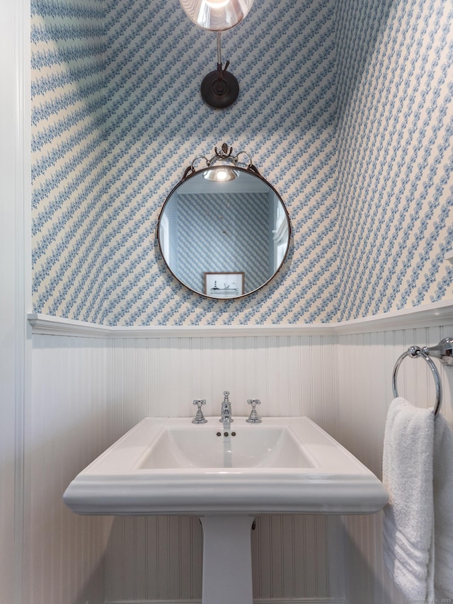 bathroom featuring wallpapered walls, wainscoting, and a sink
