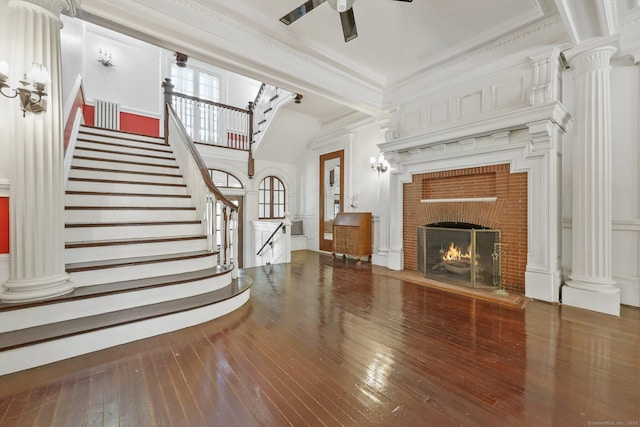 unfurnished living room with ornamental molding, ceiling fan, stairs, a brick fireplace, and hardwood / wood-style flooring