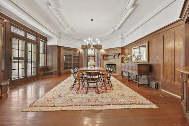 dining space featuring ornamental molding, wooden walls, a chandelier, dark wood-type flooring, and a fireplace