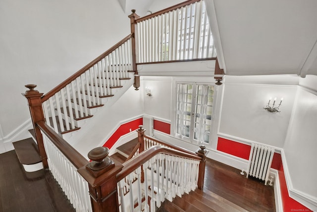 stairway featuring radiator heating unit, a towering ceiling, and hardwood / wood-style flooring