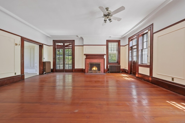 unfurnished living room featuring radiator, a fireplace, a ceiling fan, and ornamental molding