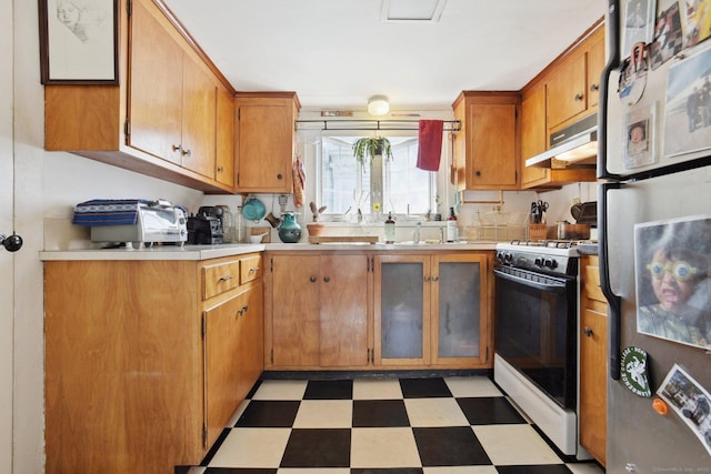 kitchen featuring white range with gas stovetop, freestanding refrigerator, light floors, under cabinet range hood, and light countertops