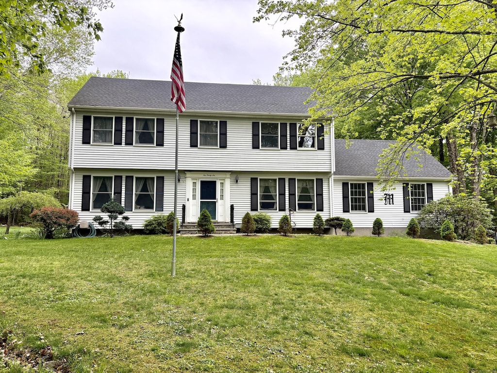 colonial home featuring a front lawn, entry steps, and a shingled roof