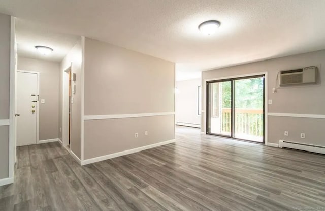 spare room featuring wood finished floors, a baseboard heating unit, a textured ceiling, a baseboard radiator, and an AC wall unit