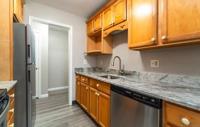 kitchen featuring a sink, brown cabinets, light wood-style flooring, light stone countertops, and appliances with stainless steel finishes