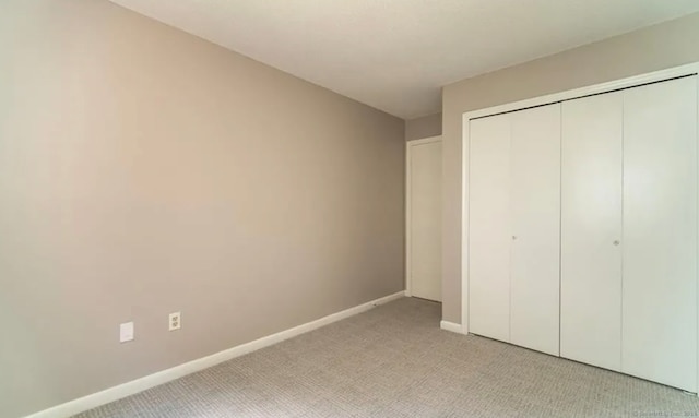 unfurnished bedroom featuring light colored carpet, a closet, and baseboards