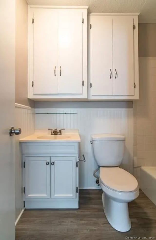 bathroom featuring toilet, vanity, a wainscoted wall, wood finished floors, and a bathing tub