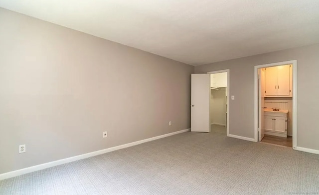 unfurnished bedroom featuring ensuite bathroom, a closet, light colored carpet, a spacious closet, and baseboards