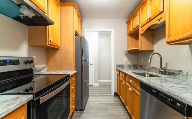 kitchen with light stone countertops, under cabinet range hood, a sink, stainless steel appliances, and light wood-type flooring
