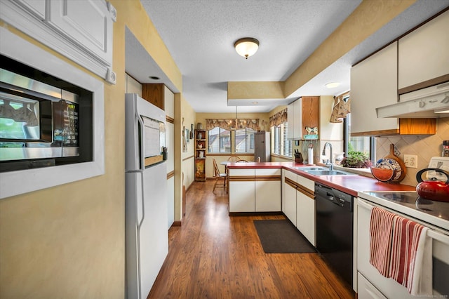 kitchen featuring white appliances, a sink, a peninsula, dark wood finished floors, and backsplash
