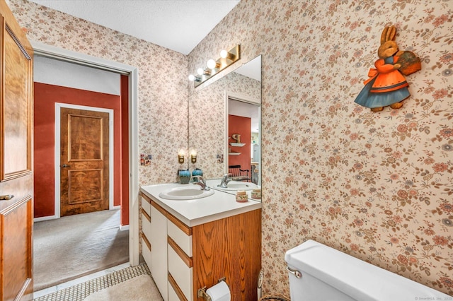 half bath with wallpapered walls, toilet, vanity, and a textured ceiling