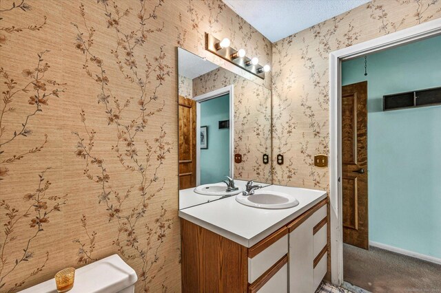 bathroom with vanity, wallpapered walls, baseboards, and a textured ceiling