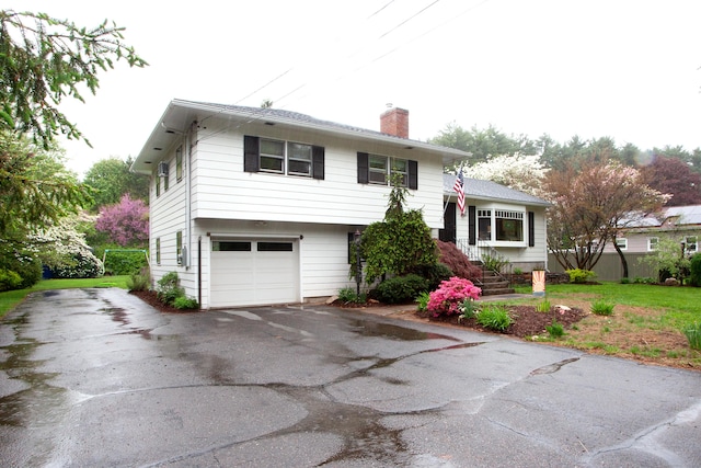 split level home with a chimney, a garage, and aphalt driveway