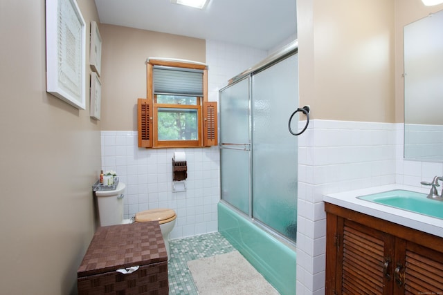 bathroom featuring tile walls, toilet, enclosed tub / shower combo, vanity, and a wainscoted wall