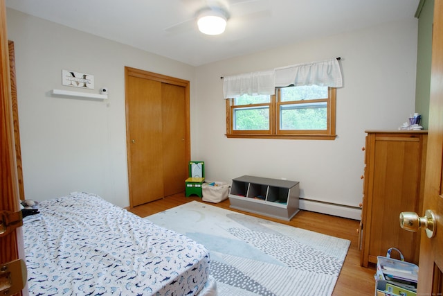 bedroom with a baseboard heating unit, light wood-style floors, a closet, and ceiling fan