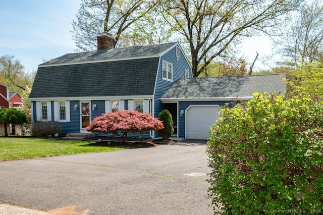 colonial inspired home featuring a gambrel roof, an attached garage, a shingled roof, a chimney, and driveway