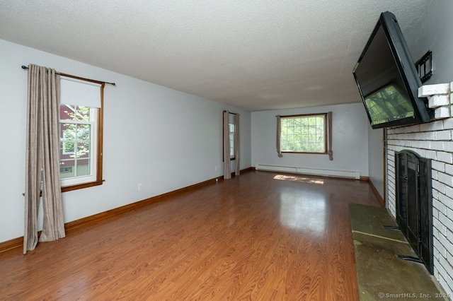 unfurnished living room featuring baseboard heating, a brick fireplace, wood finished floors, a textured ceiling, and baseboards