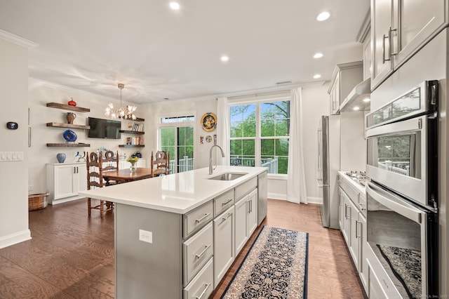 kitchen with a sink, light countertops, an island with sink, stainless steel double oven, and a chandelier