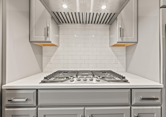 kitchen featuring range hood, stainless steel gas stovetop, gray cabinetry, tasteful backsplash, and light countertops