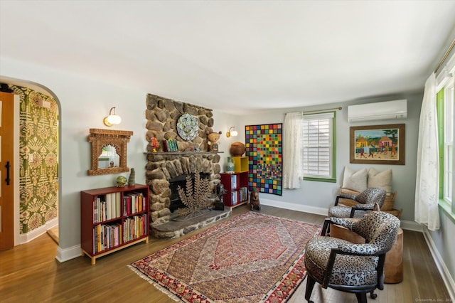 living area featuring a wall mounted air conditioner, wood finished floors, a fireplace, baseboards, and arched walkways