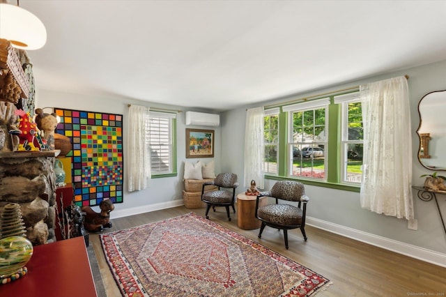 sitting room with a wall mounted air conditioner, baseboards, and wood finished floors