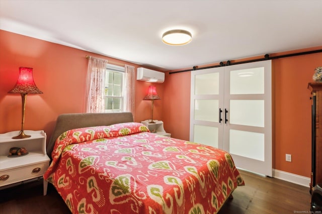 bedroom featuring an AC wall unit, wood finished floors, a barn door, and baseboards
