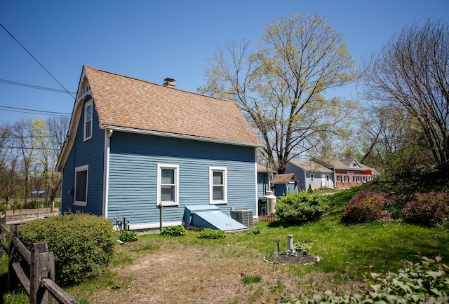 back of property featuring a chimney, cooling unit, roof with shingles, and a lawn
