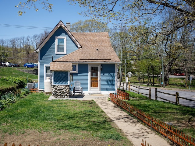 view of front facade featuring a chimney, fence, central AC, a shingled roof, and a front lawn