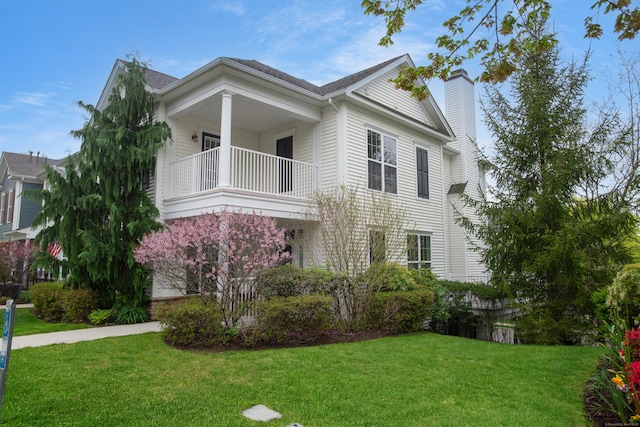 view of front facade featuring a front lawn, a chimney, and a balcony